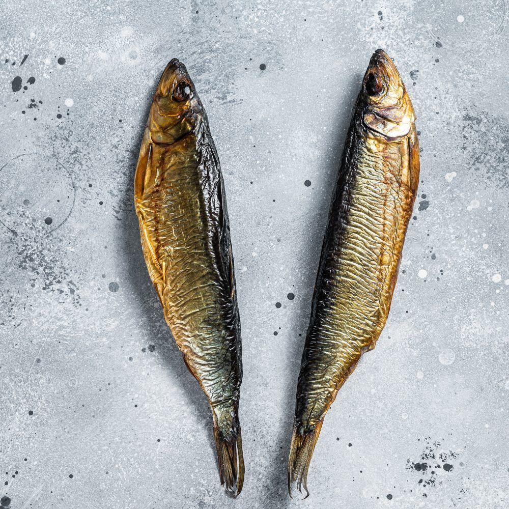 Hot smoked whole herrings on kitchen table. Gray background. Top view.